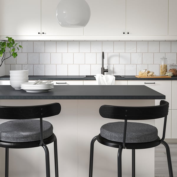 Modernt kök med 2 ÅKERVINDEFLY stolar i minnesskum. Tallrikar, skålar, ljusgrått kakel, svart bänk.