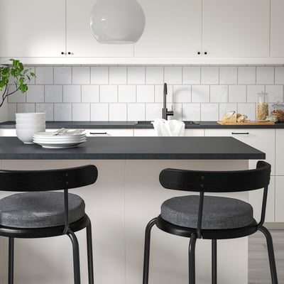 Modernt kök med 2 ÅKERVINDEFLY stolar i minnesskum. Tallrikar, skålar, ljusgrått kakel, svart bänk.