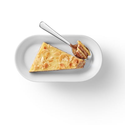 Skiva mandelgräddkaka med flingor på vit tallrik och gaffel, krämig och krispig konsistens.