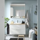 Modernt badrum med ljusblått kakel, vitt skåp och bänkskiva i bambu; Handdukar och växter synliga.