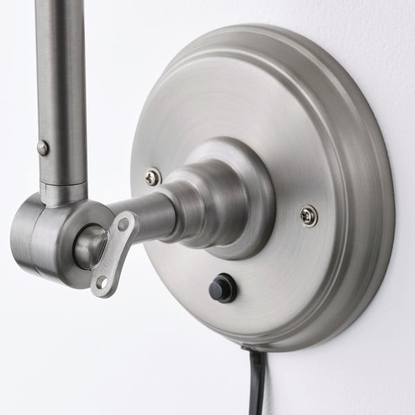 Silverjusterbar vägglampa med borstad yta och flexibel arm, monterad på en rund bas. Omkopplaren är placerad på sidan av basen.