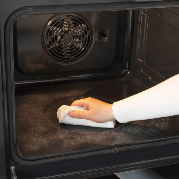 Personen rengör insidan av ugnen i rostfritt stål med en trasa. Självrengörande funktion och fingeravtrycksresistent yta synlig.