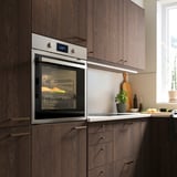 Modernt kök med inbyggd ugn i rostfritt stål med skåp i mörkt trä, digital display och mat på gallret.