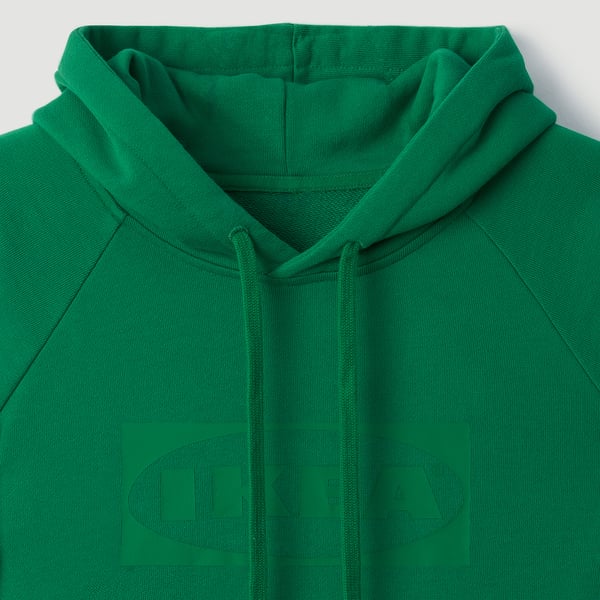 Grön hoodie närbild, slät struktur, huva med dragsko, framficka, diskret logotyptryck.