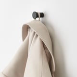 En beige handduk hänger på en svart krok som är fäst på en ljus vägg.