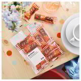 Öppnade chokladkakor BELÖNING på träbord med vinglas, tallrik, kopp, blommor, konfetti.