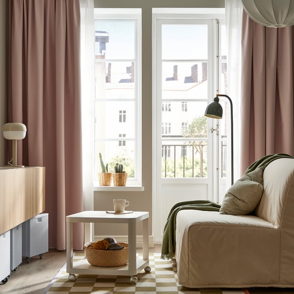 Stora, mjuka rosa BENGTA-gardiner ramar in ett rum med en bekväm soffa under ett högt fönster och erbjuder en mysig och väl upplyst atmosfär.