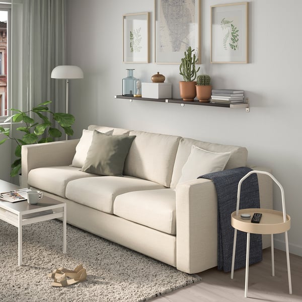 Minimalistiskt vardagsrum med beige soffa, växter och gröna gardiner.