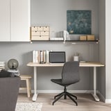 Hemmakontor med skrivbord i trä, bärbar dator, ergonomisk stol, väggkonst och bokhylla.