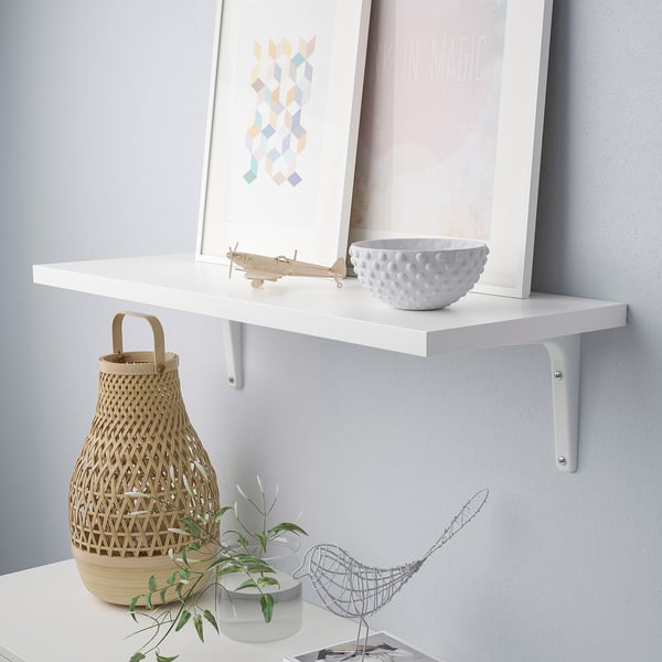 Vit vägghylla med flätad korg, liten skål och inramad konst. Modern display med flera användningsområden.