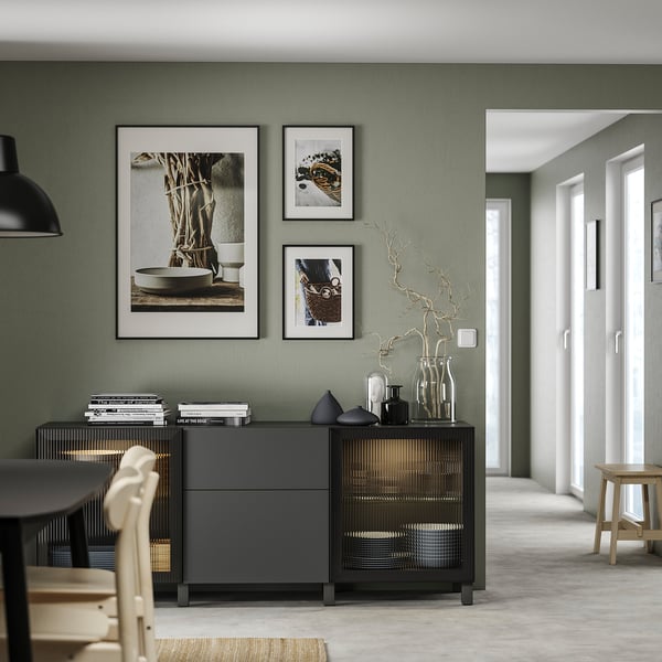 Modernt vardagsrum med grå förvaring BESTÅ, med flyttbara hyllplan, svarta vaser och inramad konst på salviagrön vägg.