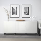 Vitt BESTÅ-sideboard med justerbar toppdisplay, inklusive vinglas och skål, i kombination med urbana tryck med svart ram.