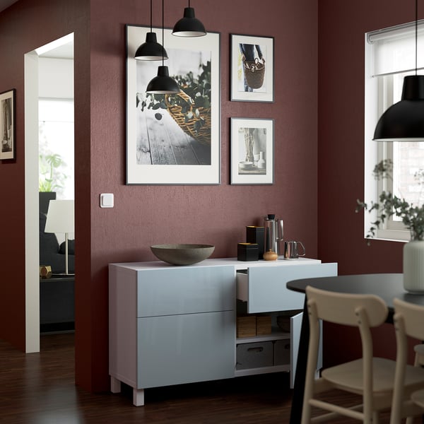 Vitt BESTÅ sideboard med lådor och hyllor, som visar dekorativa föremål, placerat under väggmonterade foton och hängande lampor.