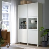 BESTÅ vitrinskåp nära fönster, med flyttbara hyllor och växt.