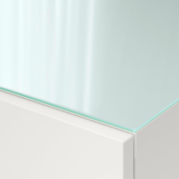 Närbild av en elegant topppanel i härdat glas på en vit BESTÅ-enhet. Glaset är klart och reflekterande, vilket säkerställer en enhetlig, blank finish.