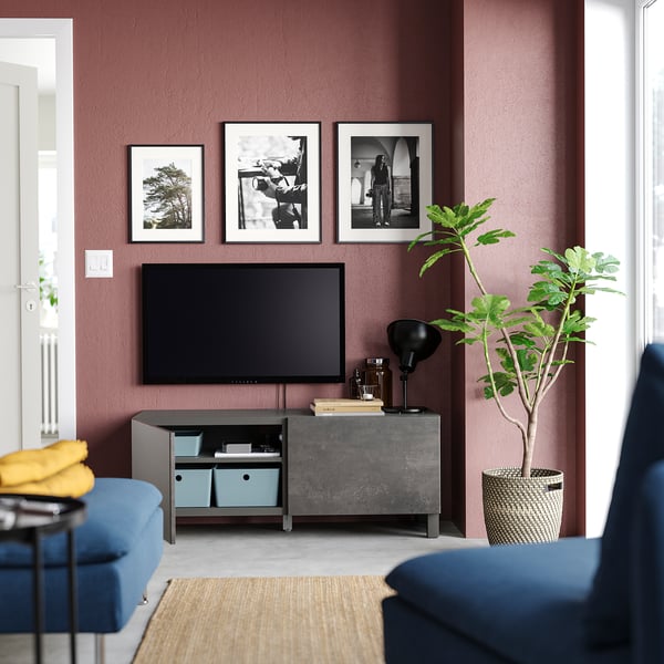 Modernt vardagsrum med rödbruna väggar, blå soffa, plattskärms-tv på mörkgrå BESTÅ tv-bänk, inramad konst och krukväxt.