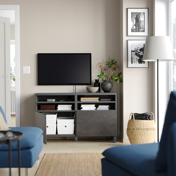 Modernt vardagsrum med TV-bänken BESTÅ, blå soffa, plattskärms-tv, lampa, vävd korg och svartvita foton.