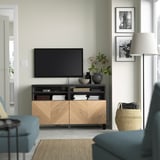 Modernt vardagsrum med tv-bänken BESTÅ, tv, böcker, vaser och konst. Blå soffor, golvlampa och korg i närheten.