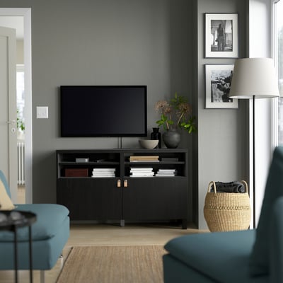 Modernt vardagsrum med BESTÅ svart tv-bänk, elegant design, gott om förvaring, plattskärms-tv, dekorativa föremål och blågröna sittplatser.