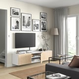 Modernt vardagsrum med vitt BESTÅ-tv-bänk, plattskärms-tv och svart soffbord. Dekorerad med svartvita foton och en hög lampa.