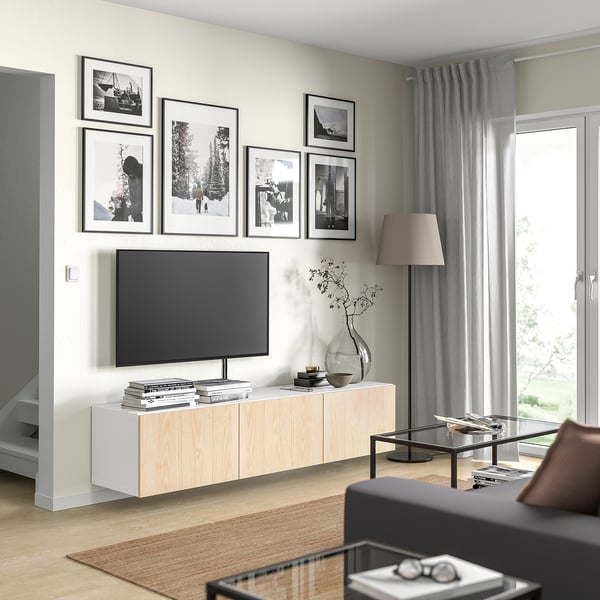 Modernt vardagsrum med tv-bänk i ljust trä, svart tv, inramade foton, grå gardiner och svart soffa.