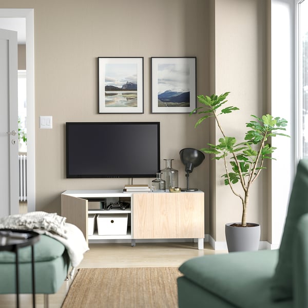 Modernt vardagsrum med ljusbeige BESTÅ-tv-bänk, gröna vadderade stolar, en krukväxt och inramade naturfoton.