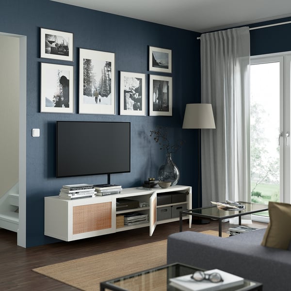 Modernt vardagsrum med mörkblå väggar, med BESTÅ-tv-enhet, plattskärms-tv, foton, soffbord i glas och stort fönster.