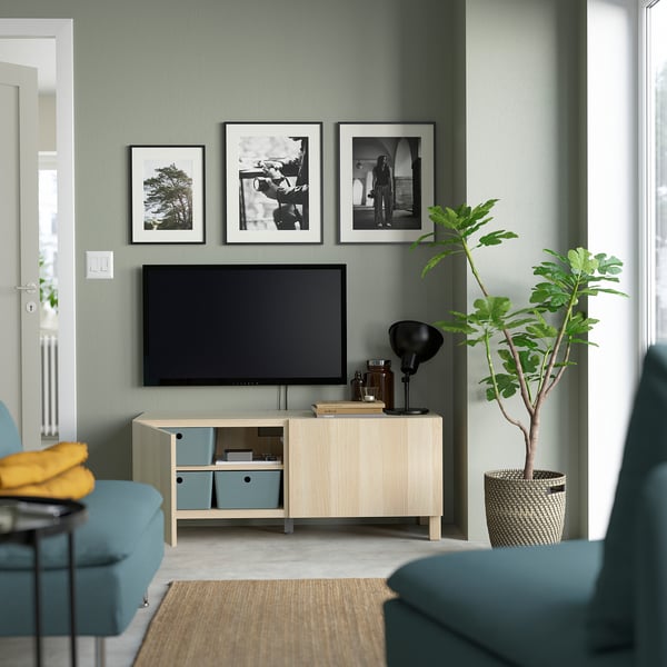 Modernt vardagsrum med gröna väggar och tv-bänken BESTÅ, flyttbara hyllor, tre foton, hög växt i korg.