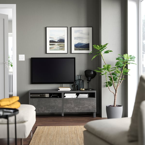 Modernt vardagsrum med grått BESTÅ tv-bänk; plattskärms-TV, inramade bergsfoton, krukväxt, vit soffa.