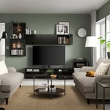 Modernt vardagsrum med gröna väggar, tv och bokhyllor. Soffbord, soffor, lampa och klocka kompletterar inredningen.