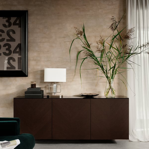 Modernt vardagsrum med mörkbrunt BESTÅ-skåp, grön stol, vit lampa, hög växt i glasvas och inramade konstverk på texturerad vägg.