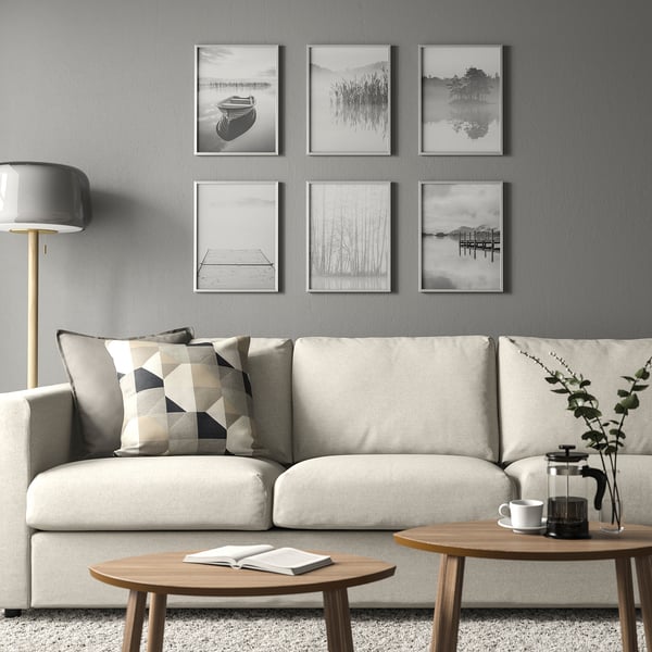 Modernt vardagsrum med vit soffa, BILD-affischer, soffbord, lampa och växt.