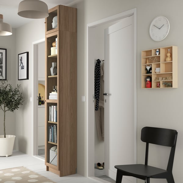 Hög BILLY bokhylla bredvid vit dörr, med böcker, vaser. Modern, minimalistisk design.