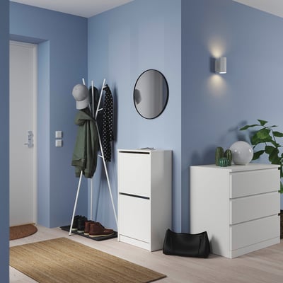 Modern blå entré med vita BISSA-förvaringsenheter, rund spegel, klädhängare och grönska.