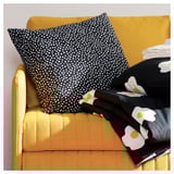 En gul soffa, en svartvit prickig prydnadskudde och en svart trasa med vita blommönster.