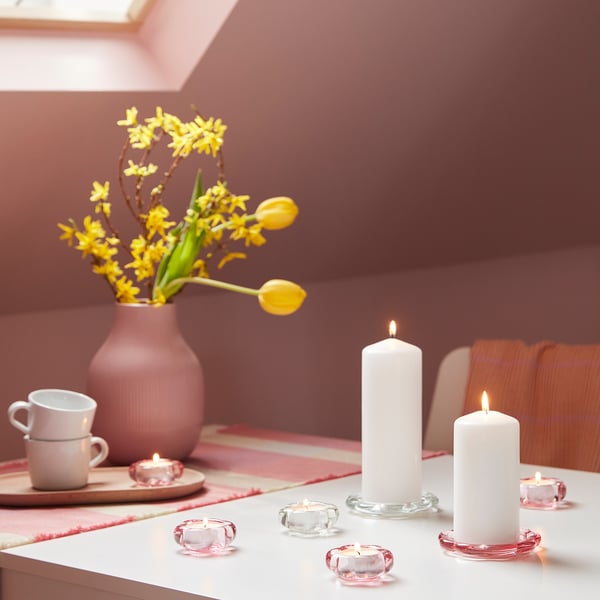 Rosa glas ljusrätter, blominspirerade, på bordet med vita ljus, gula blommor.