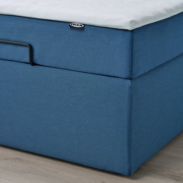 En blå ottomansk divansäng med integrerad förvaring; En närbild av basen och en lyftrem för enkel åtkomst.