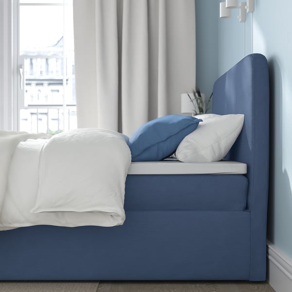 En blå ottomansk säng med en vadderad sänggavel och ett stort förvaringsutrymme under. Den innehåller en bekväm madrass med pocketfjädrar för stöd.