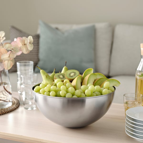 Skål i rostfritt silver med skivade gröna frukter på ett träbord.