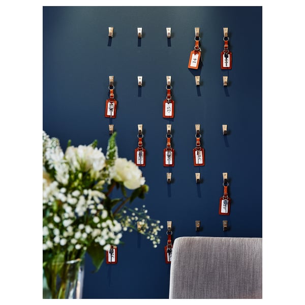 Väggdisplay med flera blå handdukskrokar och röda etiketter. Vita blommor i vas.