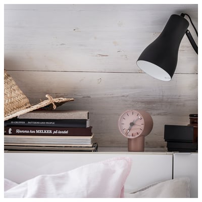 Föreställ dig en rosa BONDTOLVAN-väckarklocka på en trähylla med böcker och en lampa.