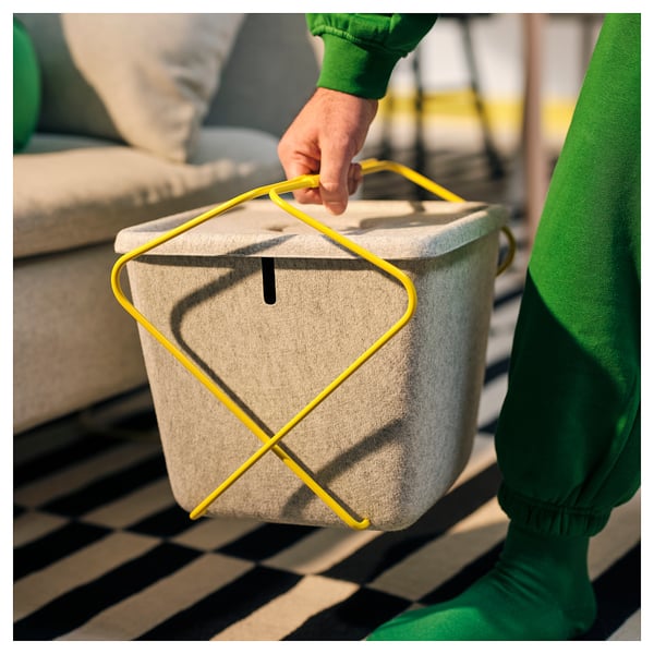 En person som bär en förvaringskorg i filt med gula handtag, lämplig för speltillbehör.