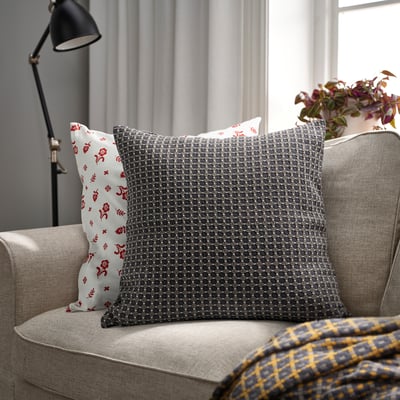 BRUNNYCKLAR grå kudde på beige soffa, större än röd blommig kudde, gulrutig filt.
