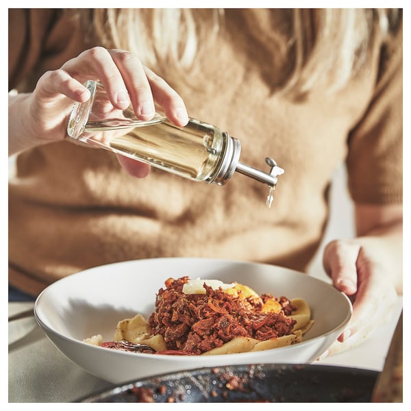 En person ringlar olja från en genomskinlig CITRONHAJ-flaska i glas på en måltid i en vit skål och visar upp ett enkelt köksredskap.