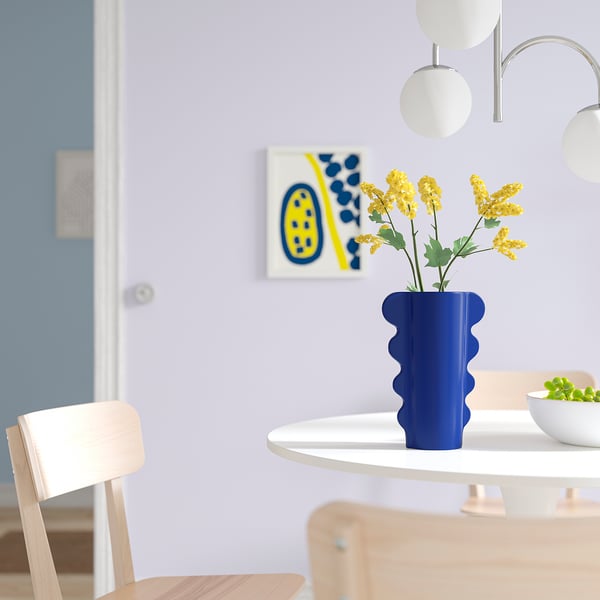 Minimalistisk matplats med blå vasen DOFTBRÄKEN, gula blommor och abstrakta konstverk.