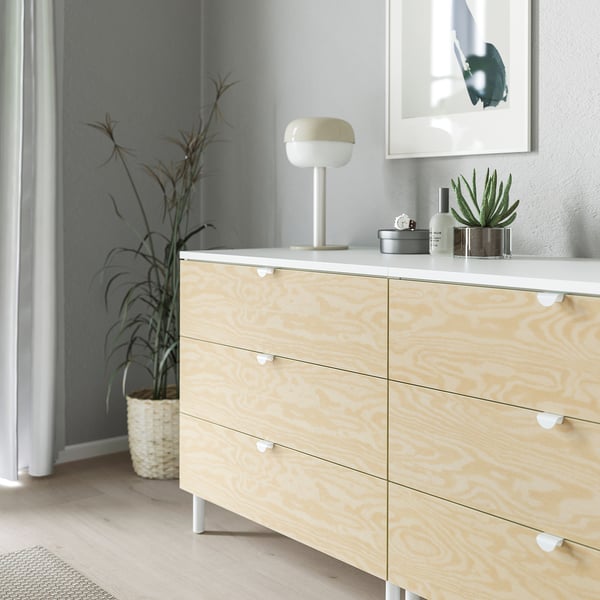 Byrå i trä med lätta knoppar och handtag; en enkel, modern design; har tre lådor, var och en med ett smidigt, rundat grepphandtag; sitter på vita ben.