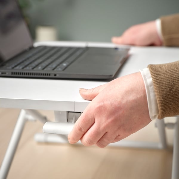 En person justerar ett DUBBLA stativ för en bärbar dator vid ett skrivbord. Stativets handtag höjer den bärbara datorn till ögonhöjd för bättre hållning.
