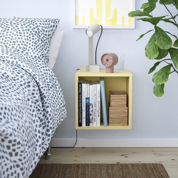 Sängkant: gul EKET kub rymmer böcker, klocka, glas. Blått överkast med vita kuddar. Plantera på sidan. Gul konst ovanför.
