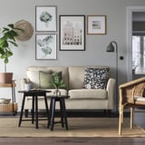 Modernt minimalistiskt vardagsrum: beige soffa EKHOLMA, svart sidobord, korgstol, grå matta, gröna växter, väggkonst.