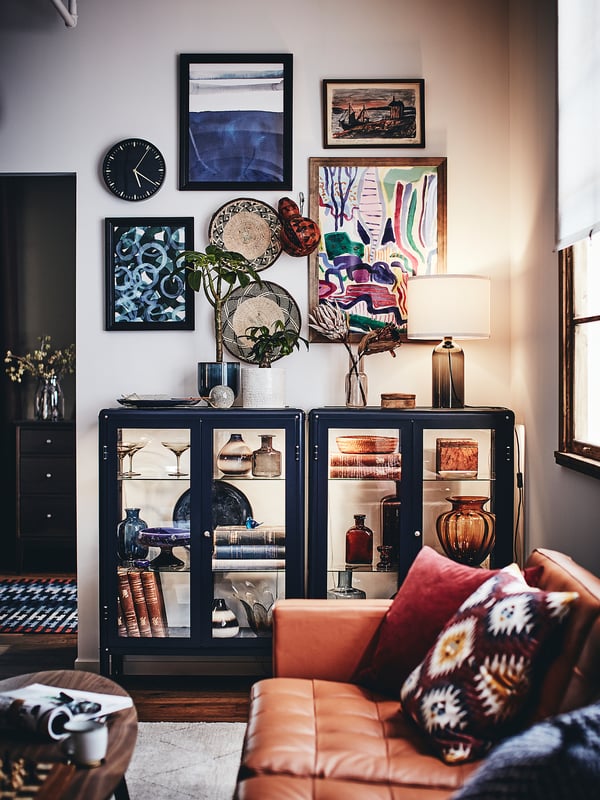 Modernt vardagsrum med orange lädersoffa, mönstrade kuddar, svart vitrinskåp med färgglada vaser, konst och en lampa.